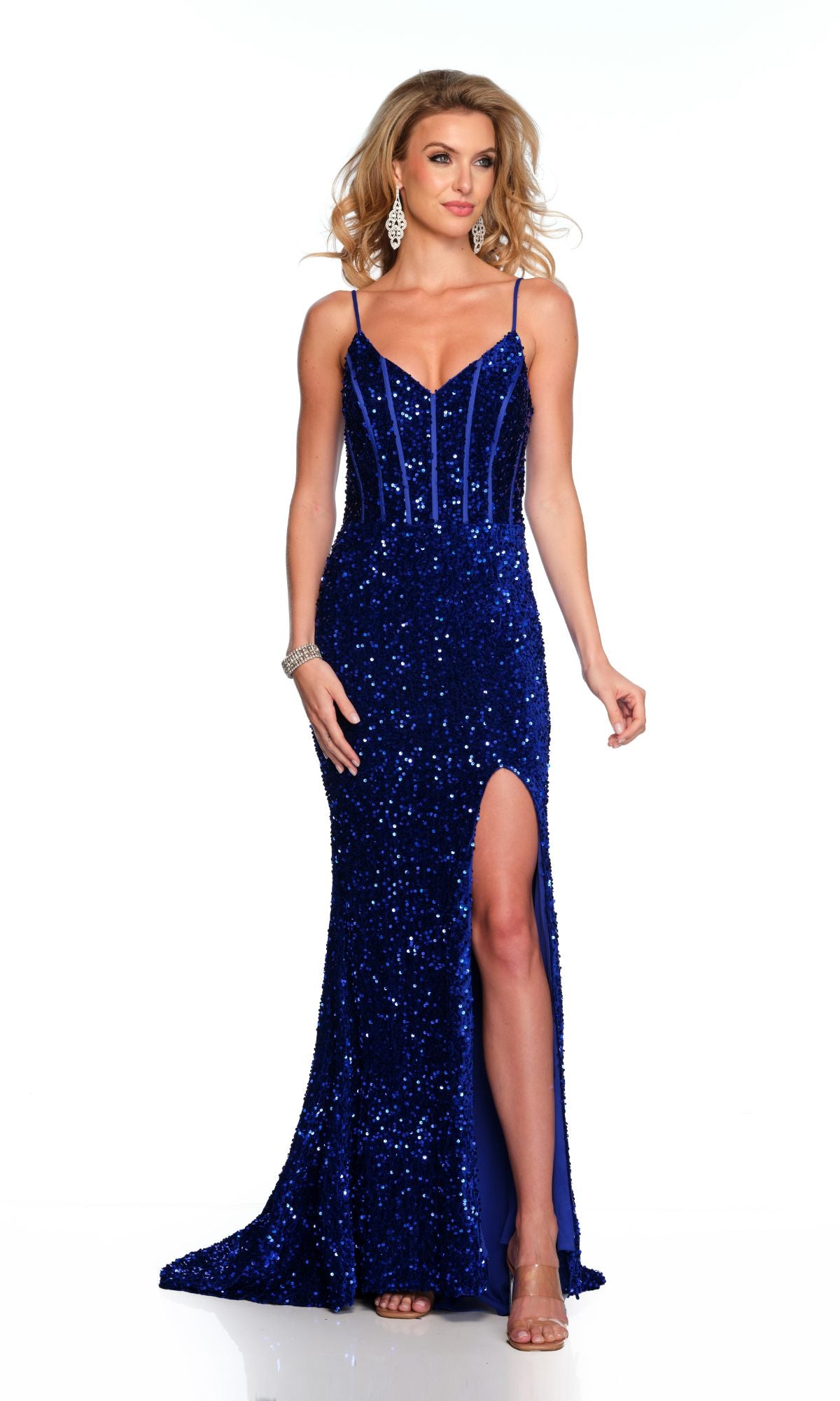 A woman stands against a white background wearing the Long Formal Dress 11652 by Dave and Johnny— a sleeveless, fitted royal blue sequin gown with a v-neck, thin straps, thigh-high slit, and silver accessories.